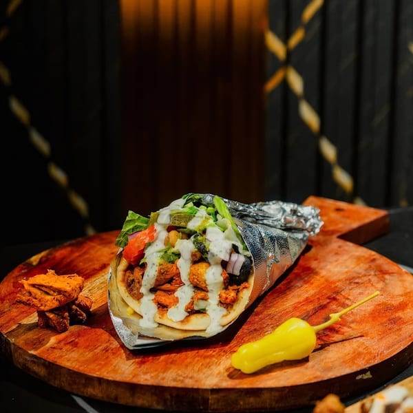 A chicken shawarma wrap with white sauce, lettuce, and tomatoes on a wooden board.