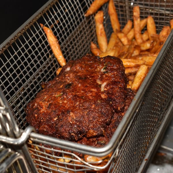 Crispy fried meat and golden french fries in a metal deep fryer basket.