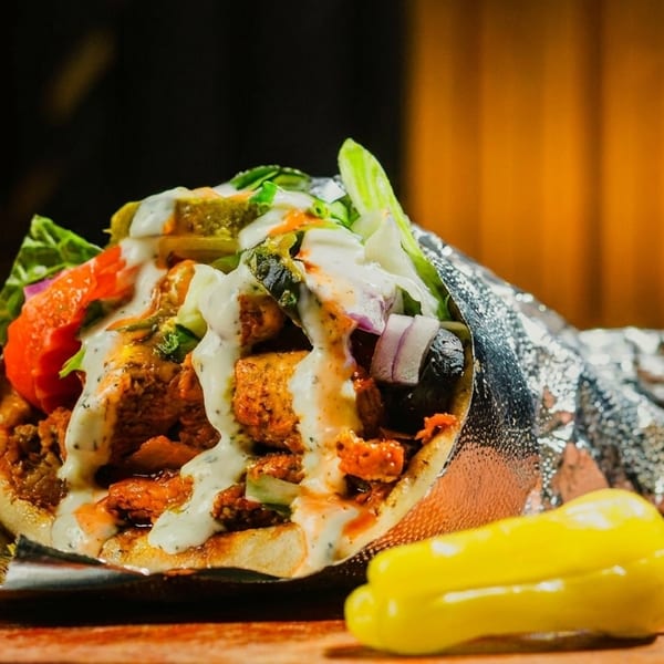 A chicken shawarma wrap with white sauce, lettuce, tomatoes, and onions, served with a yellow pepper.