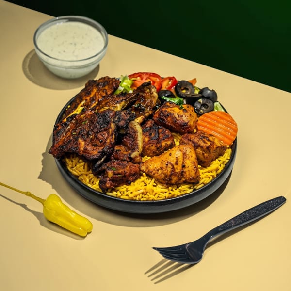 Grilled chicken and rice platter with salad, olives, carrots, and a side of white sauce.