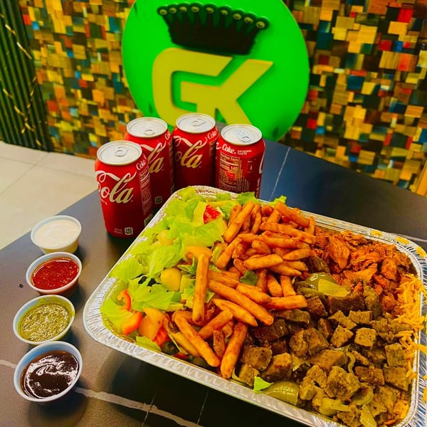 A large platter of fries, salad, chicken, and beef with four Coca-Cola cans and dipping sauces.