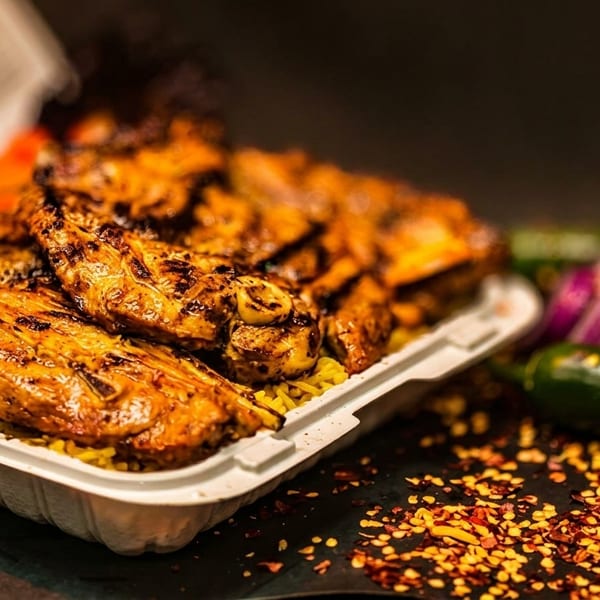 Grilled chicken and rice with chickpeas, carrots, and pickled vegetables in a takeout container.