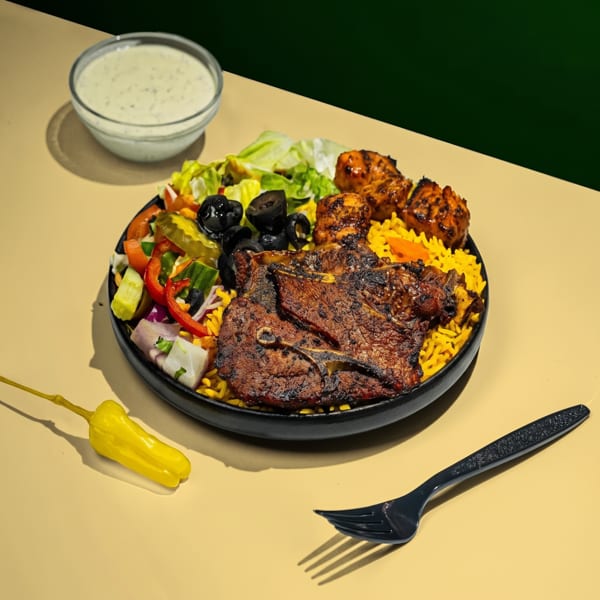 A black plate of grilled lamb chops, chicken, yellow rice, salad, and a side of white sauce.