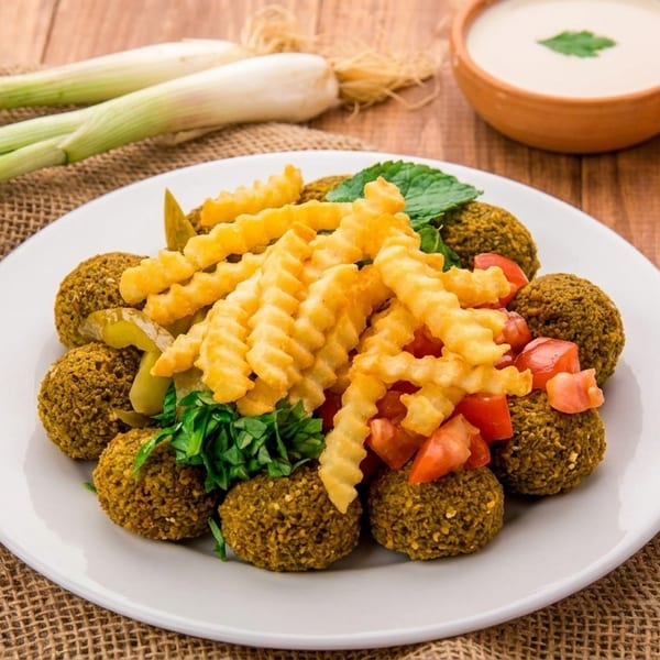 Falafel plate with crinkle-cut fries, diced tomatoes, pickles, and herbs, with sauces and scallions.