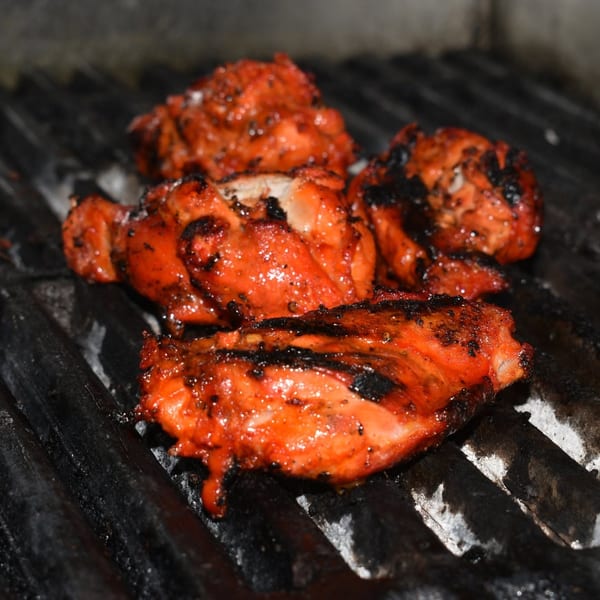 Red marinated chicken pieces cooking on a dark grill with some char marks.