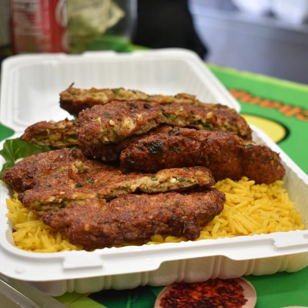 Golden yellow rice topped with crispy brown fritters, some revealing green vegetable filling, in a takeout container.